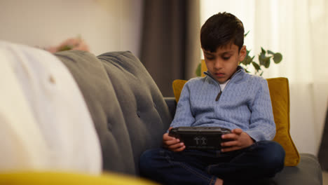 Young-Boy-Sitting-On-Sofa-At-Home-Playing-Game-Or-Streaming-Onto-Handheld-Gaming-Device-5